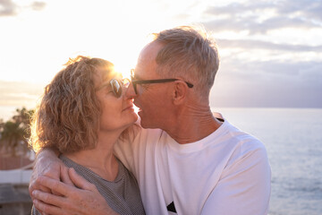 Lovely mature and romantic senior couple embrace at sunset on the seashore, two smiling people stay together expressing love and tenderness