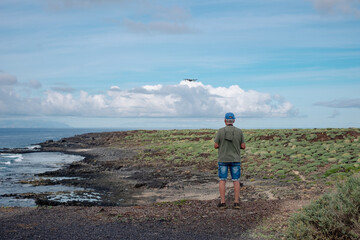 Rear view of active man guiding drone flight along sea coast. People and weekend tourism, leisure and outdoor activity lifestyle. Ocean and southern coast of Tenerife, Punta Rasca natural park