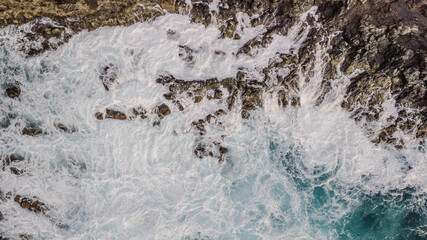 Drone view of Atlantic ocean waves meet with underwater pointed rocky. Blue rough sea with big waves with foam crashing against the rocks, south of Tenerife, Canary island