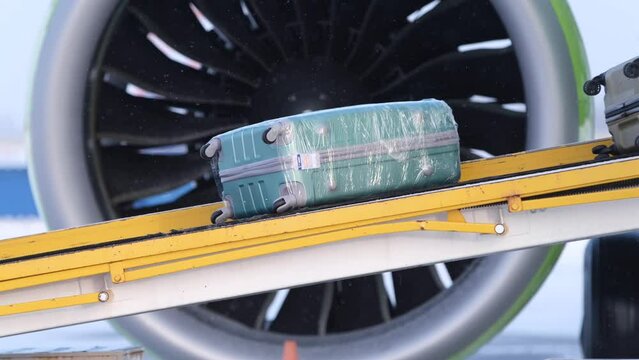 Suitcases ride on the luggage belt on the plane against of a turbine. 