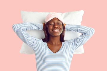Happy young african american woman wearing sleep eye mask and sleepwear isolated on a studio pink...