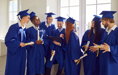 Happy smiling diverse multiethnic graduate students in blue graduation robes celebrate graduation...