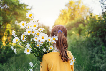 Little girl in yellow t-shirt carries huge bouquet of white flowers on her shoulder outdoors on...