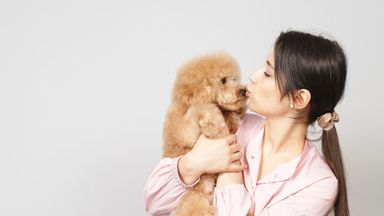 A cute and caring groomer or veterinarian hugs a little poodle puppy. Concept of caring for pets and treating them well. Place for text.