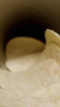Vertical video. Corn chips, hyperbolic paraboloid in shape, are scattered from a can onto the table against a black background. Dolly slider, close up.