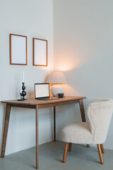 A minimal table scene of laptop with blank screen, candles, lamp on wooden table, blank photo frames on the wall. Modern inspiring apartment. Internet, social media, technology concept.