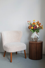 Bright fresh flowers in a ceramic vase on a stylish coffee table next to trendy chair in a minimalist living room.