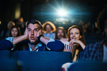 Man looking shocked watching a movie in the cinema with audience in the background