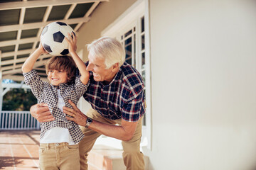 Grandfather and grandson having fun with soccer ball on the porch