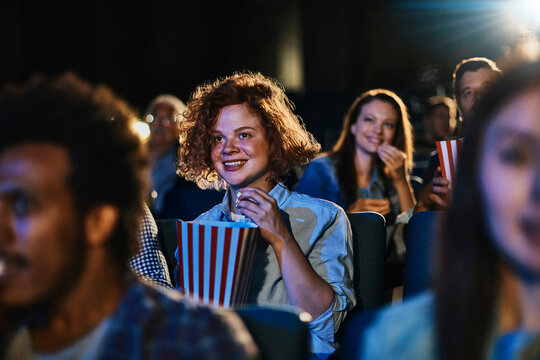 Smiling young woman watching a movie with popcorn at cinema