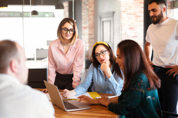 Diverse colleagues gather in office to discuss financial statistics together while looking in laptop