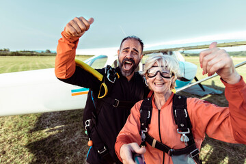 Happy senior woman and skydiving instructor celebrating successful jump with airplane in background