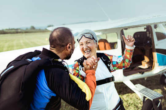 Happy senior woman and skydiving instructor celebrating successful jump with airplane in background
