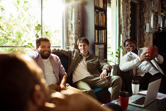 Young men sitting on a couch and having a discussion while working in a startup company office