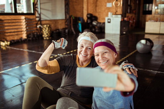 Two smiling senior women taking selfie in indoor gym