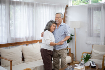 Asian senior couple embracing enjoy dancing and smiling together in the living room. Retired people do activity at home. Love and bonding of grandparents. Healthy living and insurance concept
