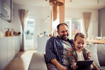 Father and daughter enjoying time together using a tablet on the sofa