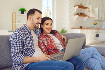 Smiling couple relaxing on the sofa at home, with a laptop. Family smiles reflect a joy as they navigate the online internet realm together. Captures the comfort of modern connectivity.