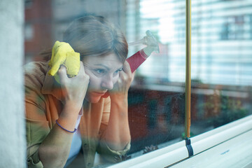 Woman cleaning window looking tired and stressed