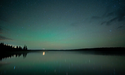 A bright green sky is colored by widespread weak Aurora at a northern lake.  The sky and millions...