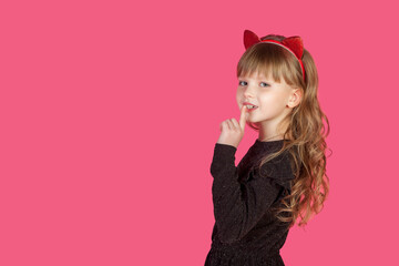 Obraz na płótnie Canvas Perfect little cover girl 7 year old with index finger by mouth at pink isolate background, looking at camera. Lovely kid lady model in cat image studio shot. Child emotion concept. Copy ad text space