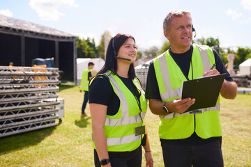 Naklejka premium Male And Female Production Team With Headsets Setting Up Outdoor Stage For Music Festival Or Concert