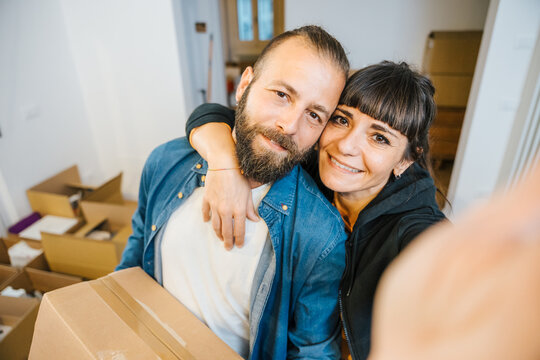Couple in love takes a selfie with smartphone in the new home, in the background the moving boxes