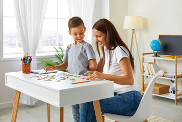 Obraz na płótnie Canvas Smiling mom and son playing board game at home. Loving mom and little daughter playing logic strategy board game at table together. Educational activity, early development at home