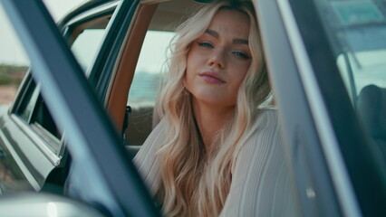 Relaxed girl chilling car looking camera close up. Blonde sitting in retro auto.