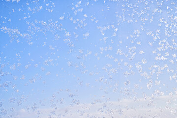 Abstract winter background. Frost on a frozen window against the blue sky.