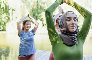 Group of teenages is engaged in fitness on pier by the lake or river. Young and positive girls go...