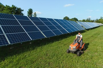 A man mows the grass near the solar panels. Green energy