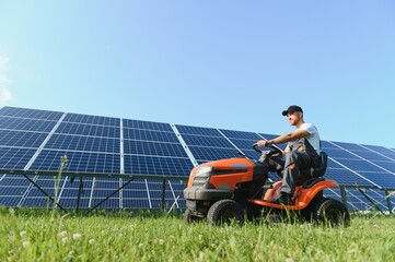 A man drives a lawnmower near solar panels. Concept of solar energy