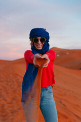 General view of a woman with a Berber scarf dropping sand from her hands from the top of a dune in the Sahara desert