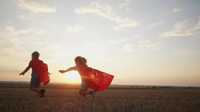 children in superhero costumes. concept of a happy childhood and family for a child. a boy and a girl with red capes and blue T-shirts are running across a field, sunset in the background lifestyle