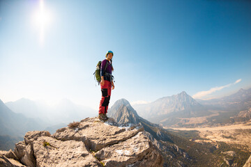 girl climber in a helmet and with a backpack stands on a mountain range against the backdrop of...