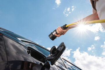 Woman opening an electric car charging socket cap and plugging in a charger