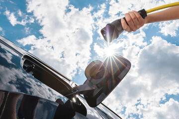 Female hand charging electric car with blue sky, photo from below