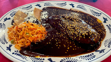 Chicken breast in mole sauce with red rice: traditional Mexican dish featuring tender chicken in rich, spicy mole sauce, served with flavorful red rice.