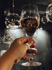 Female hand with a neat manicure holds glass of champagne. Woman raises high goblet of sparkling...
