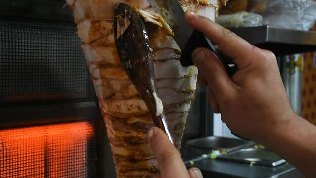 The chef prepares a shawarma sandwich by cutting toasted slices of chicken from the grill spit in a fast food restaurant.