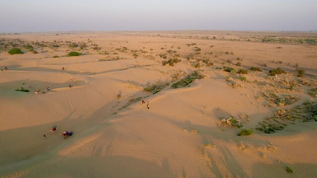 aerial drone shot flying over wide desert landscape with rolling sand dunes with tourists roaming around riding camels enjoying the tourist spot in Sam Jaisalmer rajasthan India