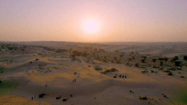 Aerial drone shot flying towards sunset over people and camels over thar desert a popular tourist destination in Sam Jaisalmer Jodhpur Rajasthan India showing landscape