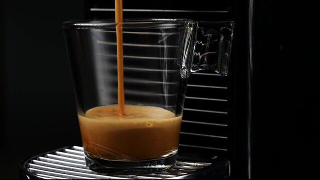 Black coffee with froth. Making black espresso or ristretto in automatic coffee machine capsules. Close up. Dark background
