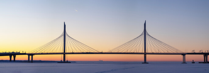 Panoramic view: Large cable-stayed expressway bridge at sunset over an ice-covered bay with an...