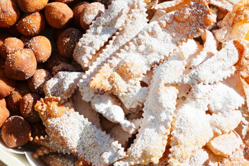 Frappe or chiacchiere with castagnole on a plate full of sugar. Typical Italian sweets of the carnival celebration. Cooked in all households and pastry shops. Also known as bugie lies
