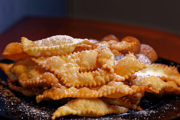 Frappe or chiacchiere with castagnole on a plate full of sugar. Typical Italian sweets of the carnival celebration. Cooked in all households and pastry shops. Also known as bugie lies