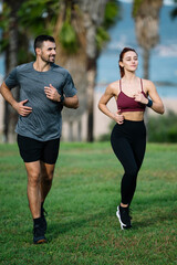 Young adult friends running together in the park jogging satisfied. Handsome athletic male and female in sportswear training workout outside.