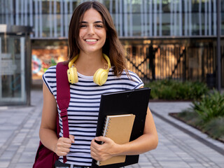 Portrait of a smiling Caucasian teenage student girl with a backpack and folder looking at camera.