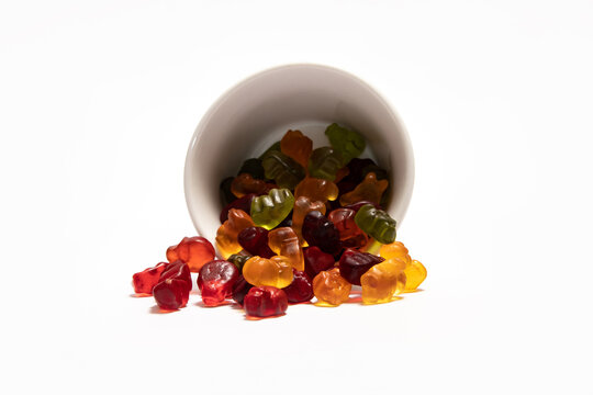 Colorful gummy candies spiled from the white cup on white background